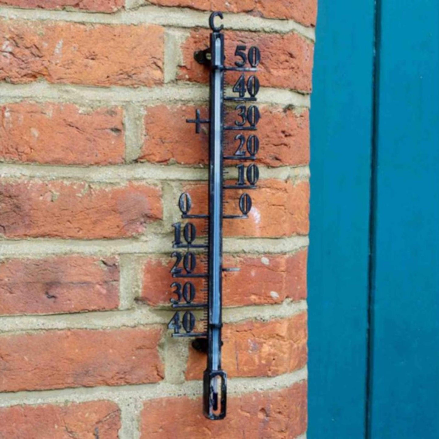 Veľký kovový nástenný teplomer od Outside In designs v exteriéri na tehlovej stene