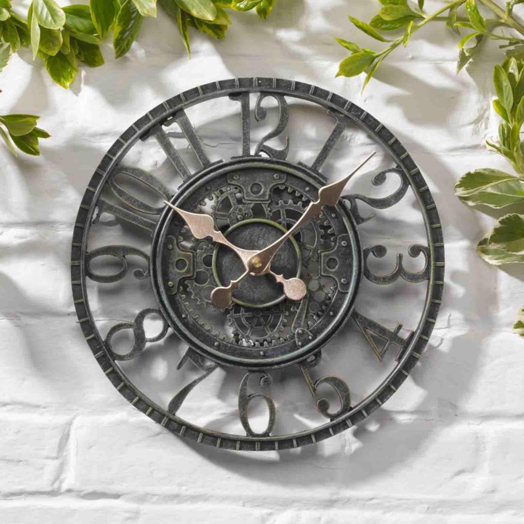 Nástenné hodiny Newby Mechanical v farbe Verdigris s priemerom 30cm na bielej tehlovej stene v záhrade