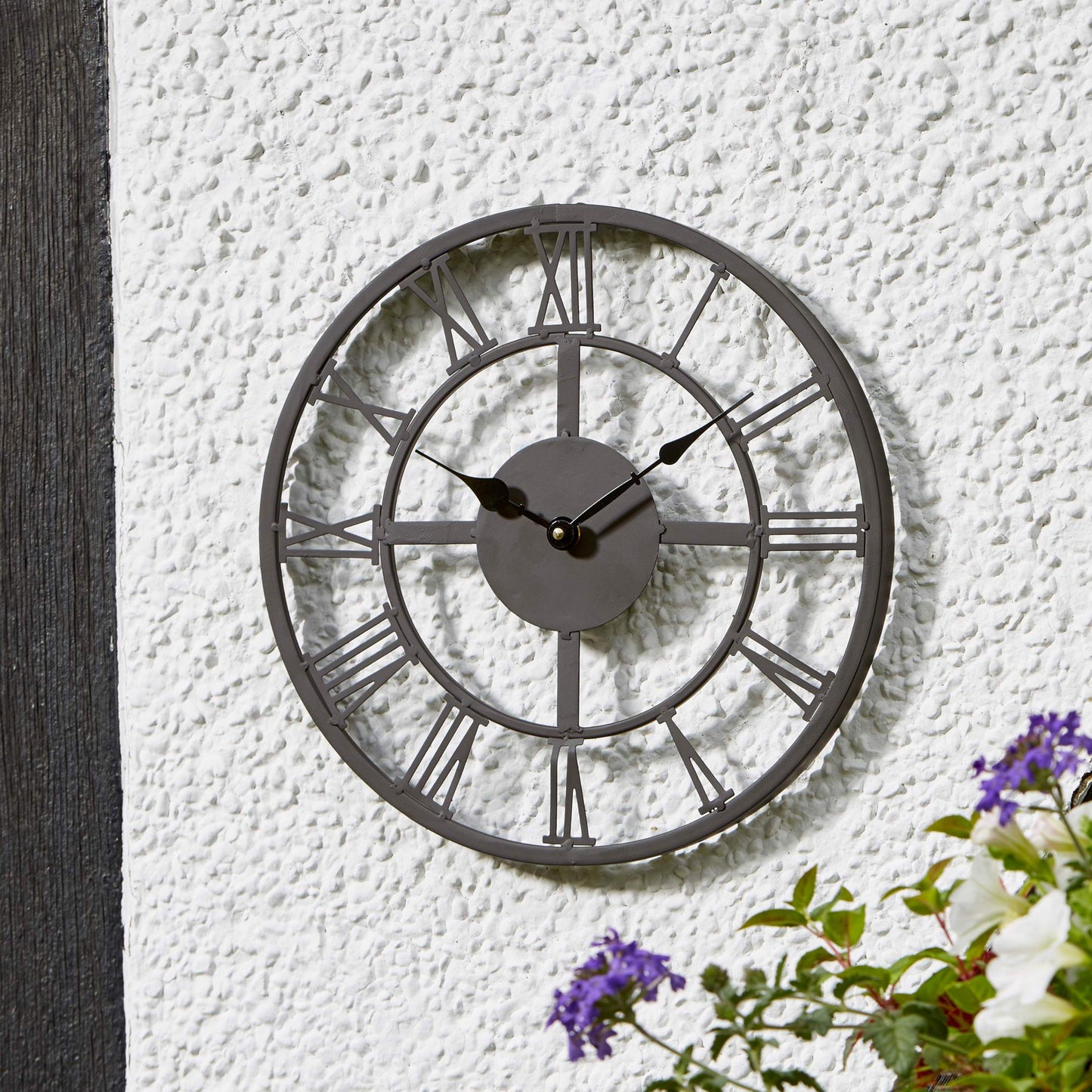 Kovové nástenné hodiny Arundel s priemerom 34cm v záhrade na omietnutej stene od Outside In designs