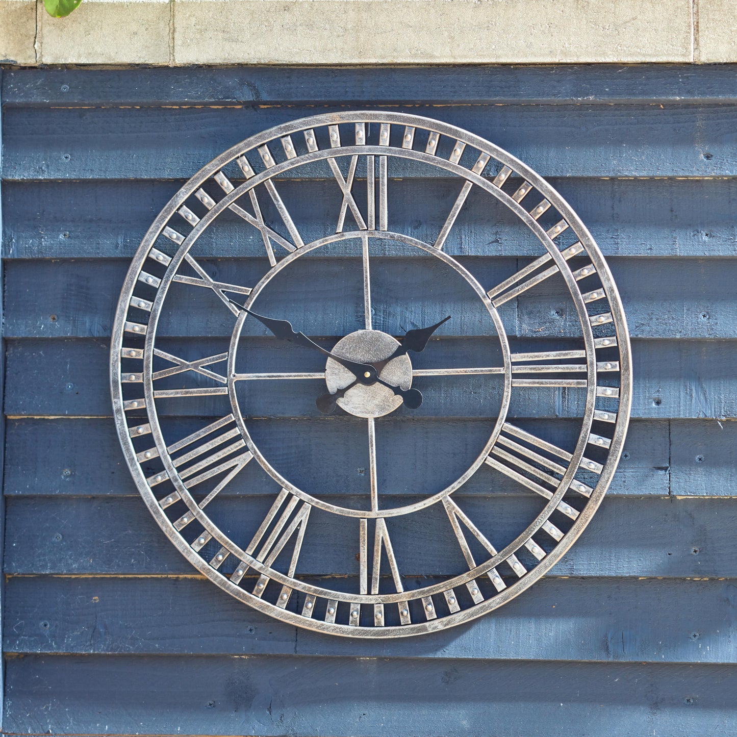Veľké kovové nástenné hodiny Buxton na drevenej stene v záhrade. Od Outside In designs