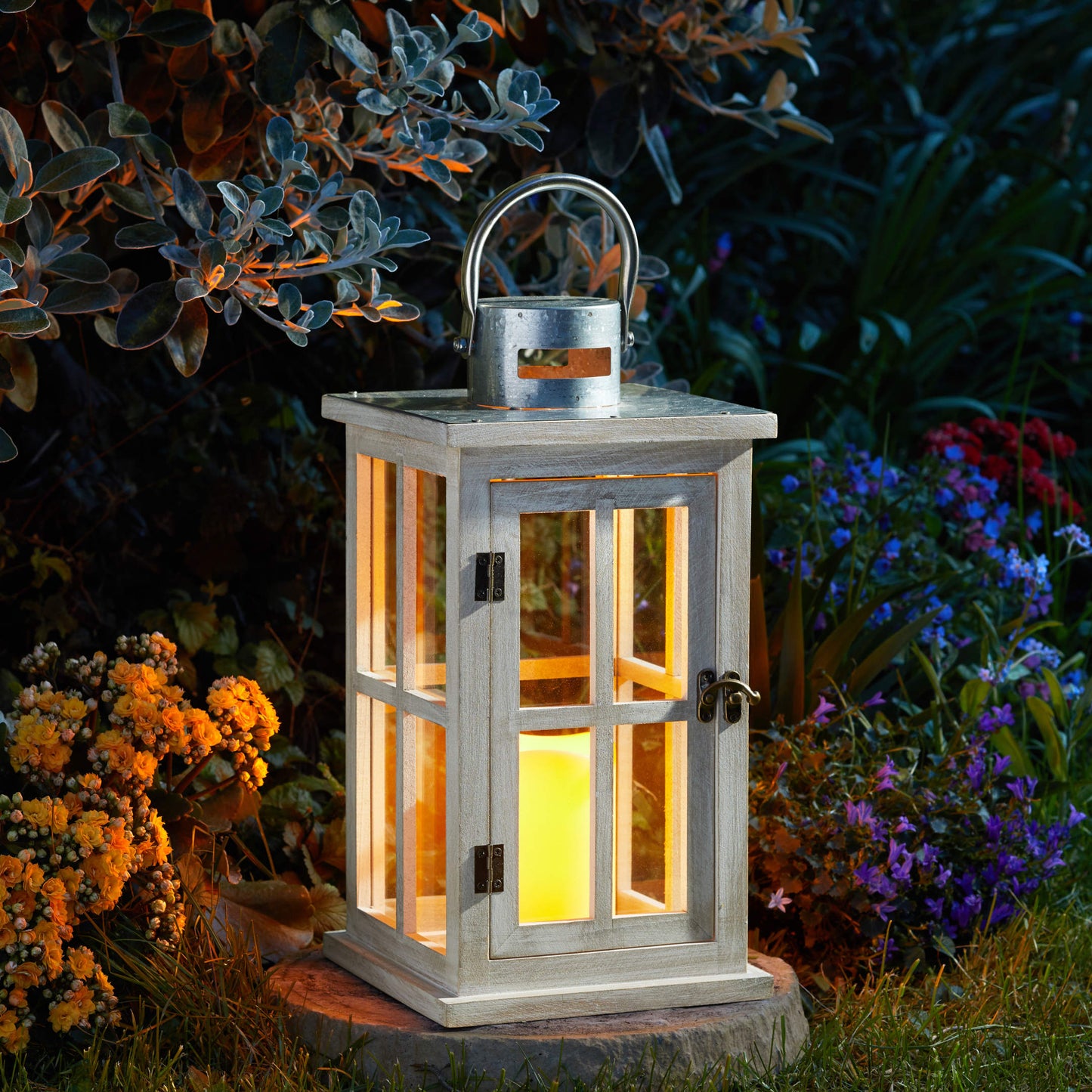 Veľký klasický drevený lampáš Skandi s kovovou strieškou s vloženou LED valcovou sviečkou v záhrade