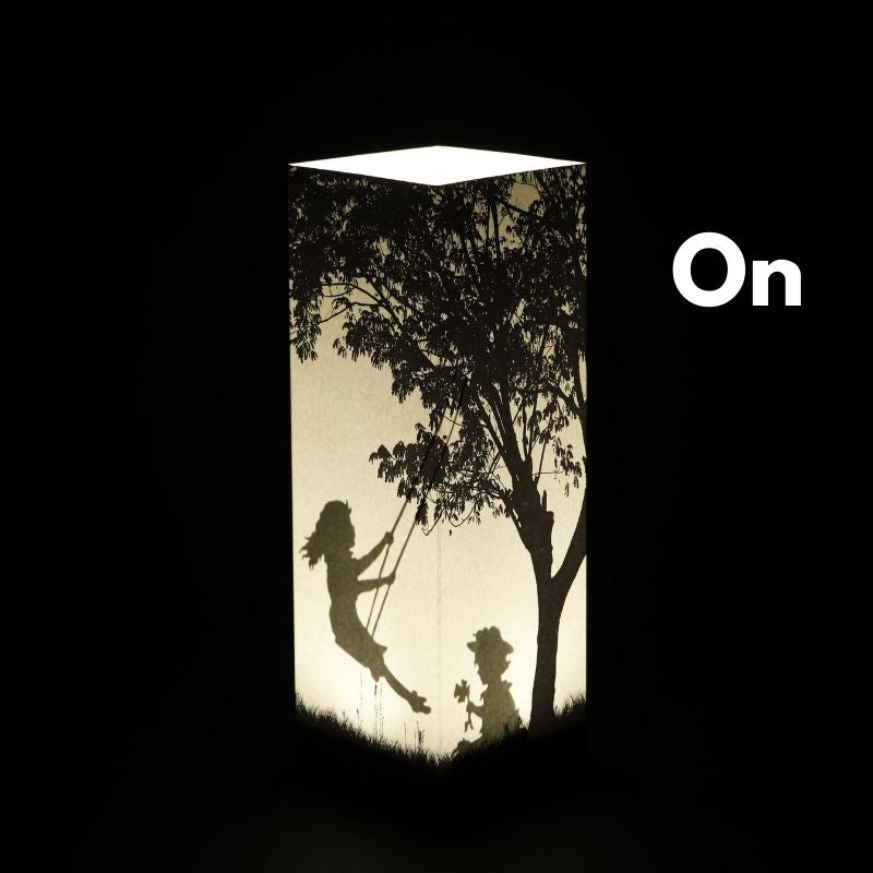 Zapnutá dekoračná tieňová LED lampa Girl on a Swing od LUXA London so siluetou dvievčatka na hojdačke